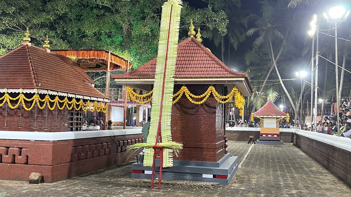 A shrine ground at night with a palm-leaf flagstaff, lights and devotees at the edge