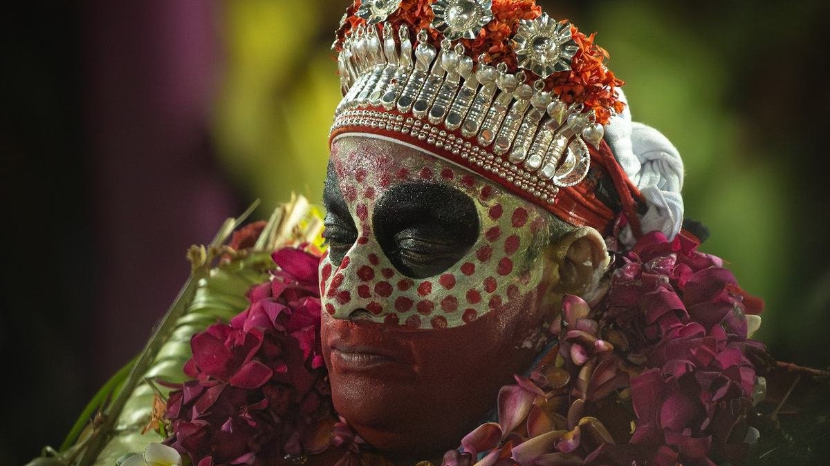 A Theyyam with a dotted white face mask and flower garlands