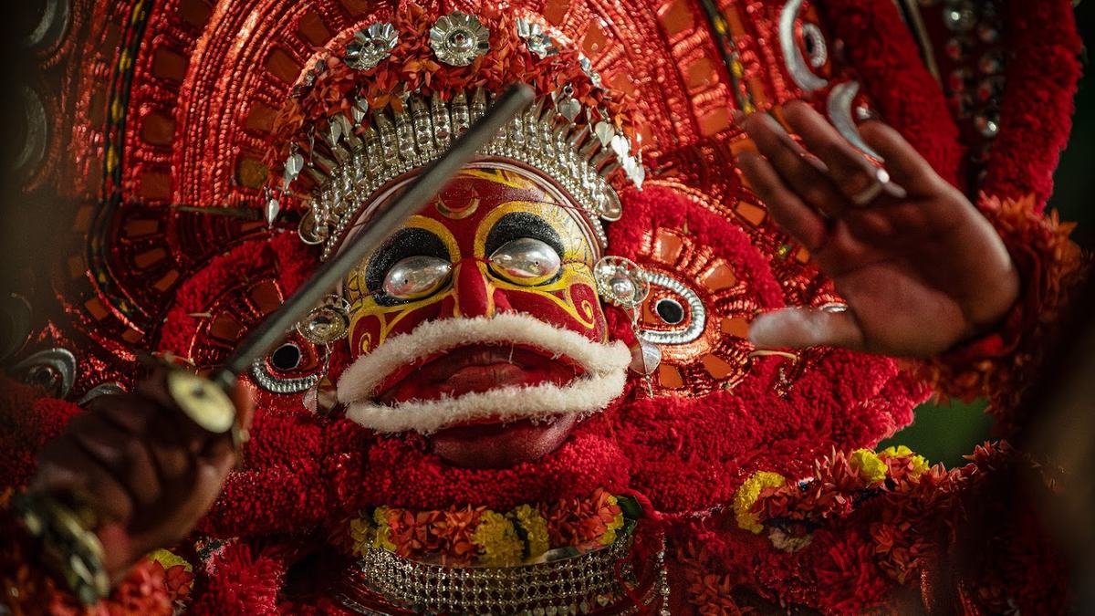 A Theyyam with a red and white painted face holding a sword