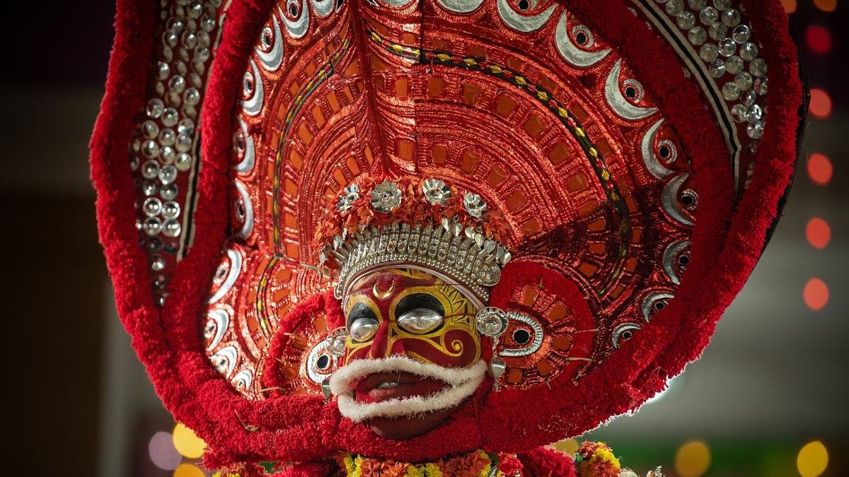 A Theyyam in a tall red headdress with a red and white painted face