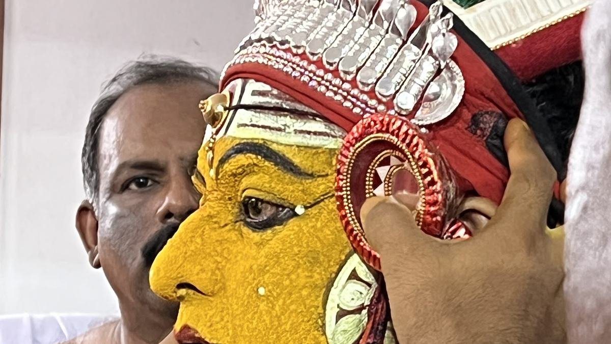 A koladhari’s yellow face being made up and the crown fitted before the ritual