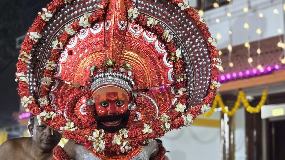 A Theyyam in a tall red headdress ringed with flowers, seen close up at night