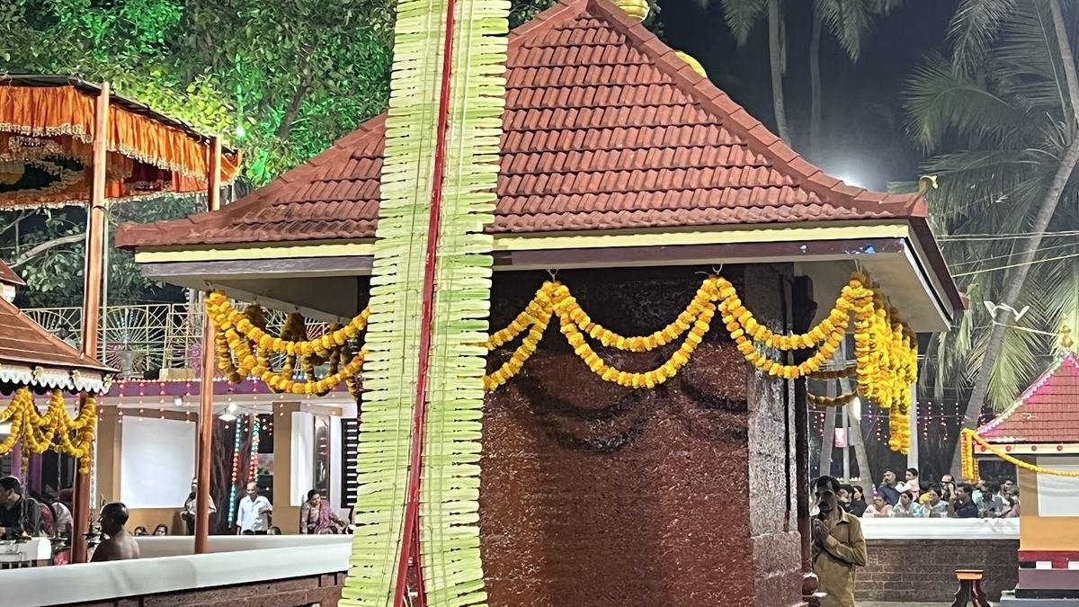 A village shrine at night with a flagstaff of palm leaves and marigold garlands