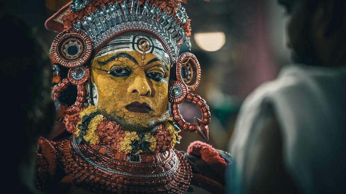 Close portrait of a Theyyam with a yellow painted face, silver crown and flower garlands