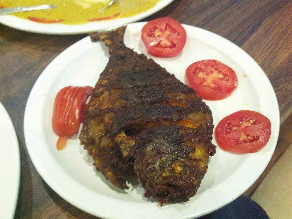 A whole fried pomfret on a plate with sliced tomatoes