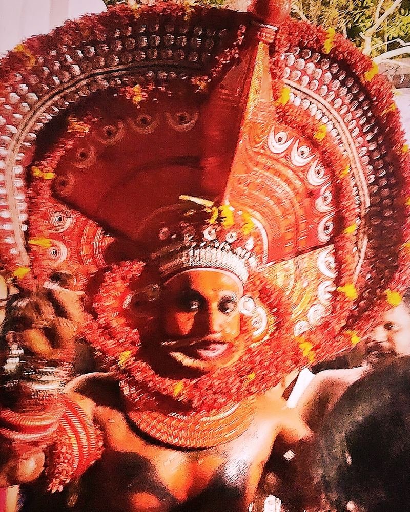 A Theyyam in a red and gold circular headdress among devotees
