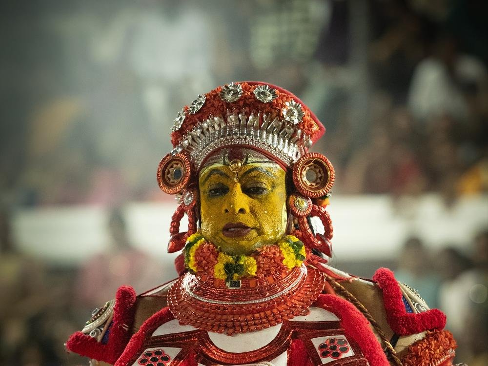 A Theyyam with a yellow painted face in red and white attire