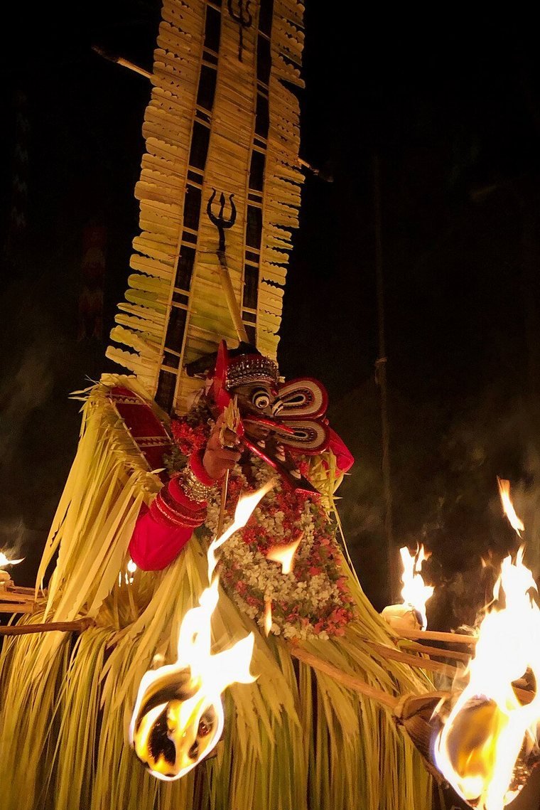 Kandakarnan Theyyam in a tall frame of palm leaf, with burning torches around the waist, at night